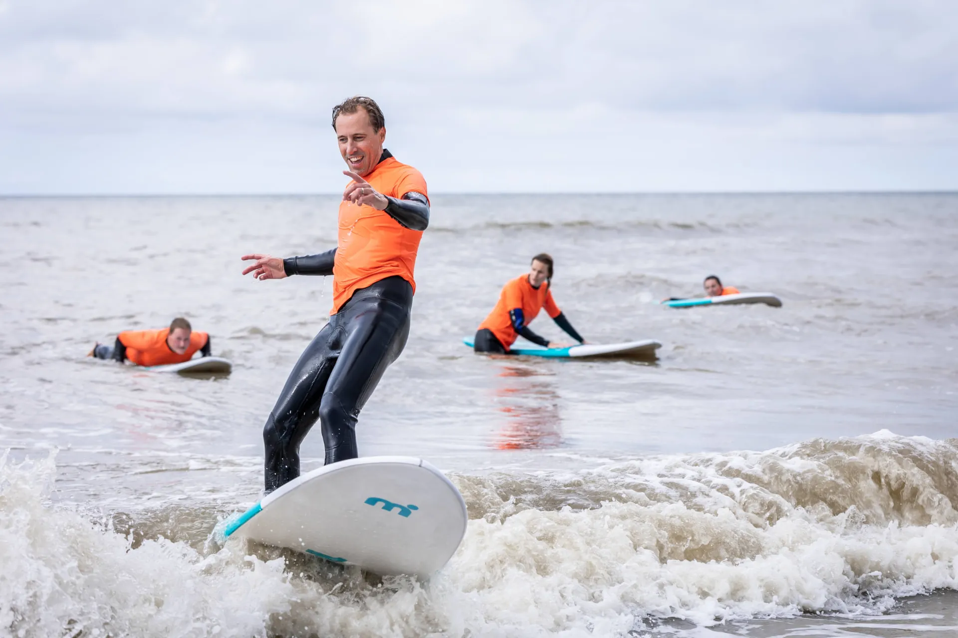 Een partner probeert op zijn surfplank te staan in de branding