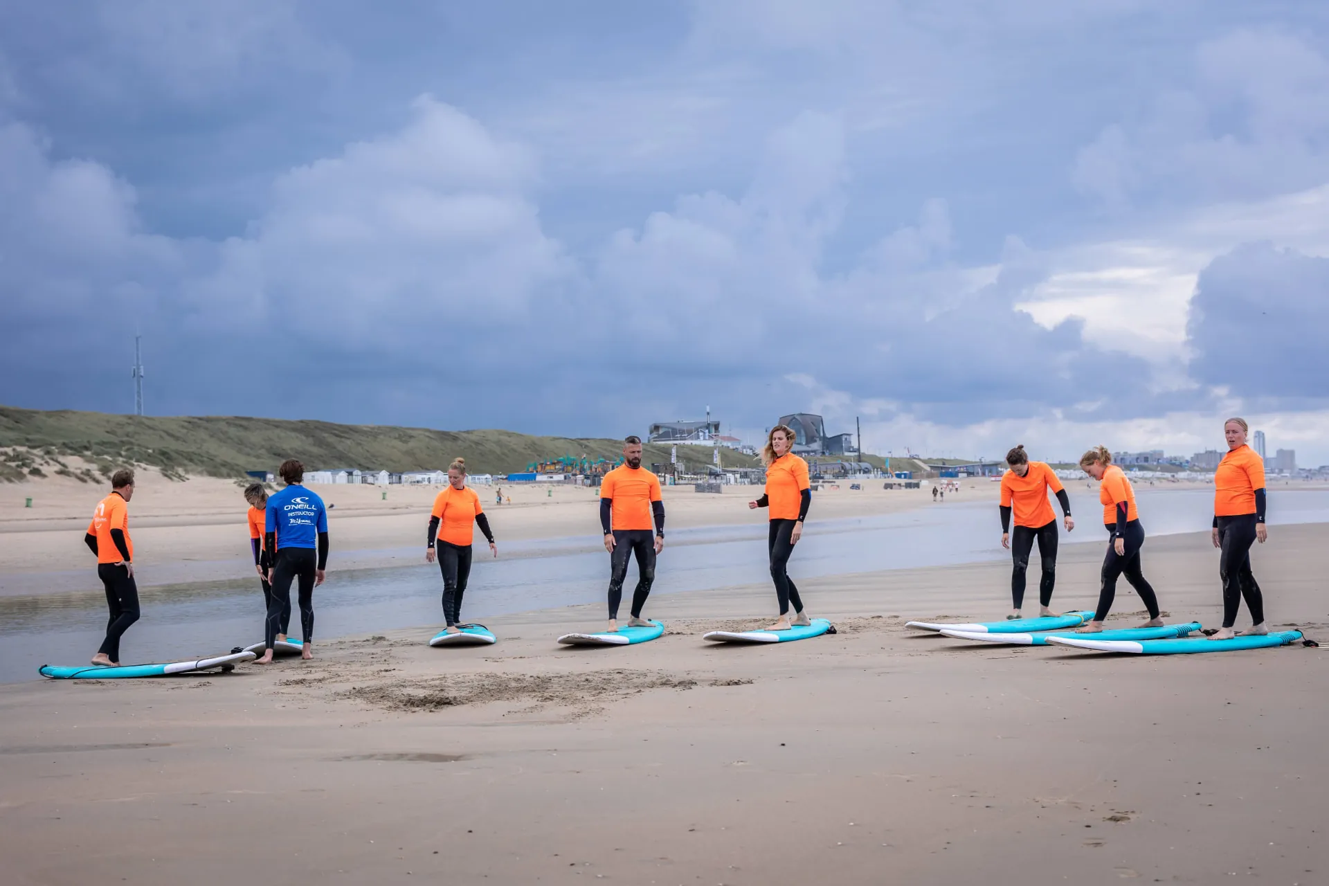 De groep staat met surfplanken verspreid over het strand